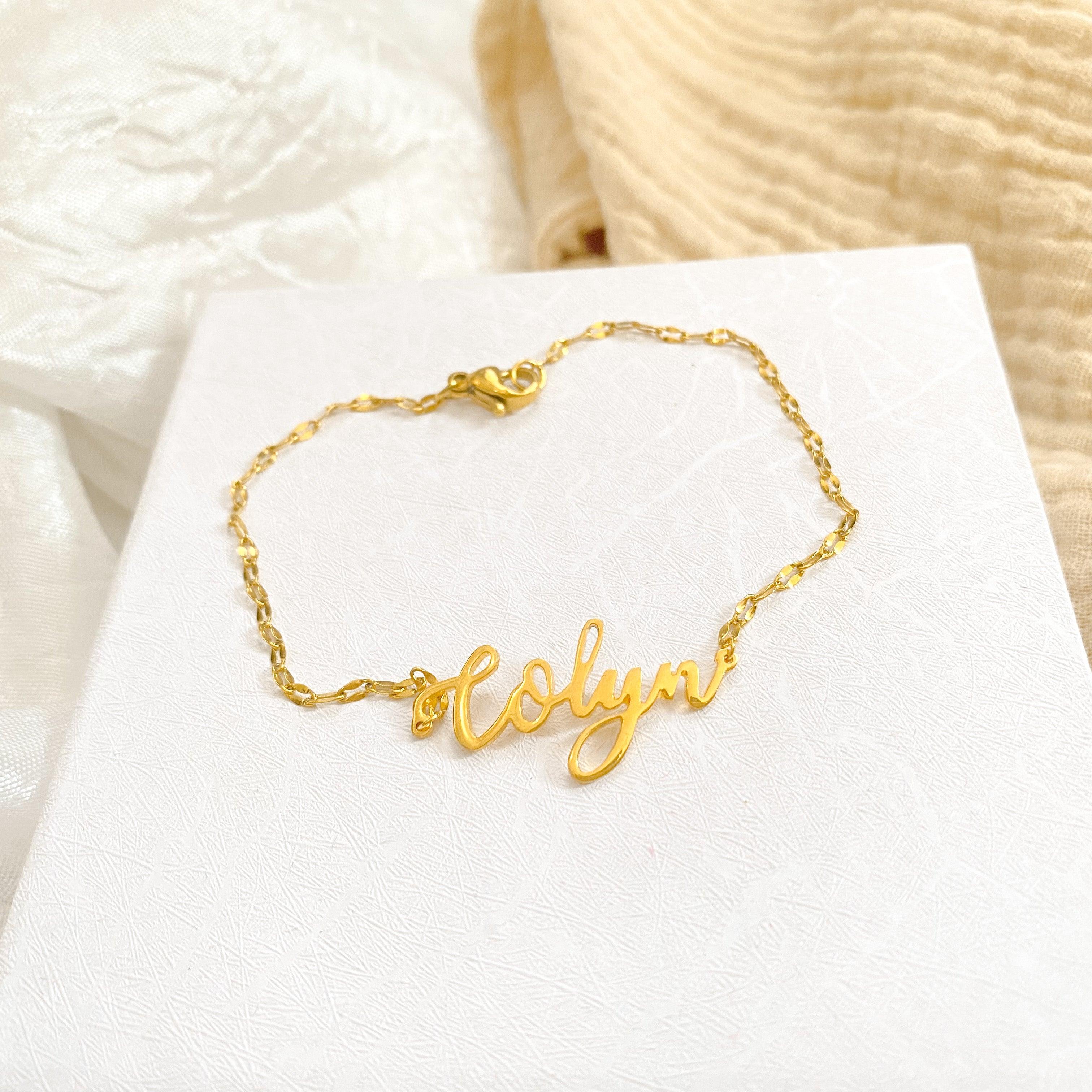 Gold script name bracelet with delicate chain on white surface